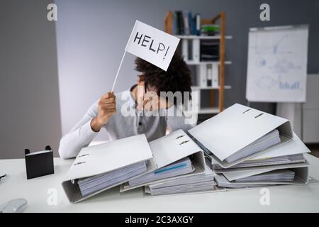 Young Unhappy Businessman Sitting And Holding White Flag With The Text Help In Office Stock Photo