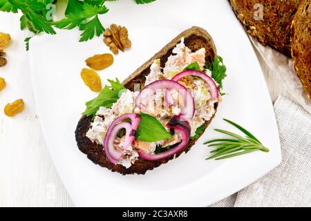 Salmon, petiole celery, raisins, walnuts, red onions and curd cheese salad on toasted bread with green lettuce on a plate on a wooden board background Stock Photo