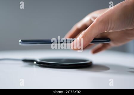 Woman Charging Smartphone Using Wireless Charging Pad At Home Stock Photo