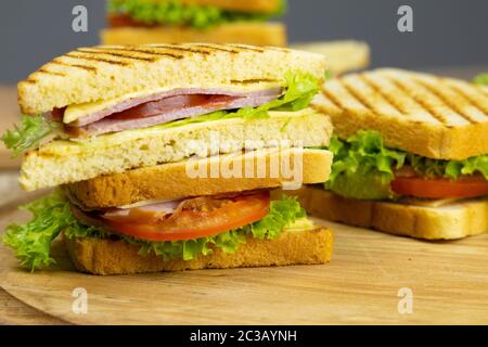 Classic club sandwich with ham and bacon on a wooden board. Next cup is a mixture of pickled miniature olives, gherkins, tomatoes. Wooden background. Stock Photo