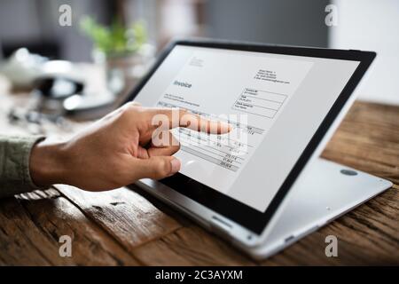 Close-up Of A Businessperson's Hand Analyzing Invoice On Laptop At Workplace Stock Photo