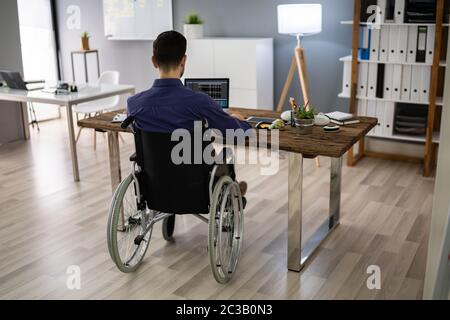 Businessman On Wheelchair While Working On Computer Stock Photo