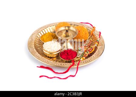 Indian Festival: Rakhi with rice grains, kumkum, sweets and diya on plate with an elegant Rakhi. A traditional Indian wrist band which is a symbol of Stock Photo