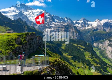 Swiss flag waving and tourists admire the peak of Jungfrau mountain on Mannlichen viewpoint, Bernese Oberland Switzerland Stock Photo