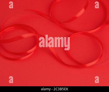 twisted red silk shiny ribbon on a red background, festive design element, close up Stock Photo