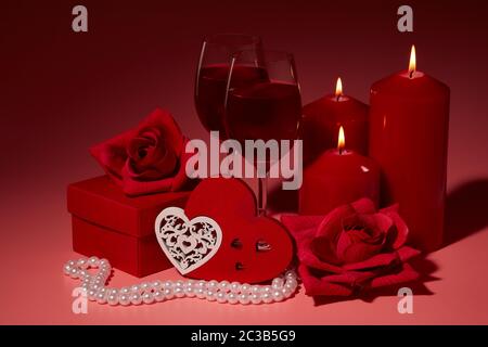 Gift boxes, two glasses with wine, burning candles, red roses and hearts on red background. Valentine's day. Wedding day.  Design element for romantic Stock Photo