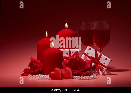 Gift boxes, two glasses with wine, burning candles, red roses and hearts on red background. Valentine's day. Wedding day.  Design element for romantic Stock Photo