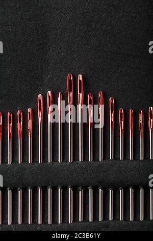 Sewing needles of different sizes in a set of red on a black background. Stock Photo