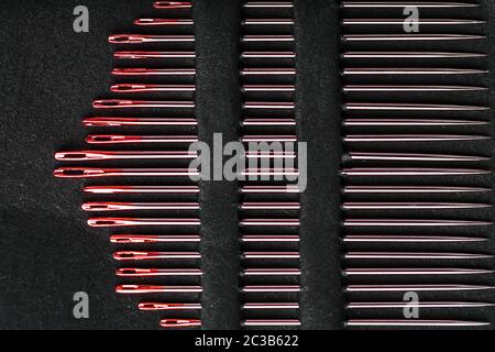 Sewing needles of different sizes in a set of red on a black background. Stock Photo