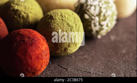 Colorful homemade truffles coated in dry beet powder, matcha tea powder, shredded cococnut on dark background. Copy space for text or design, banner. Stock Photo