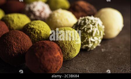 Colorful homemade truffles coated in cocoa powder, matcha tea powder, shredded cococnut on dark background. Copy space for text or design, banner. Stock Photo