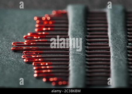 Sewing needles of different sizes in a set of red on a black background. Stock Photo