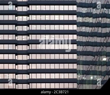 the facade of a large office urban building with rows of windows illuminated at twilight reflected in the glass facade of an off Stock Photo