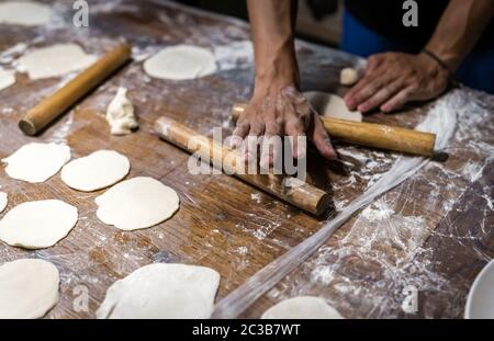 Wooden rolling pin and portioned flat dough which will be used for the making of traditional chinese dumplings during cooking class in a travellers ho Stock Photo