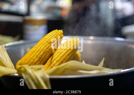 Freshly steamed corn in a metal bowl for sale on the street market in small town, China Stock Photo