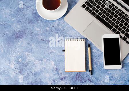 White smartphone with black blank screen on office desk with laptop, empty notebook and cup of tea. Mock up of phone. Business or education concept. T Stock Photo