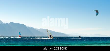 windsurfers and kitesurfers ride in the Red Sea on the background of the rocky coast in Egypt Dahab Stock Photo