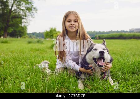 Smiling child with a pet dog husky dog play on a meadow in the summer in spring in the park. Stock Photo