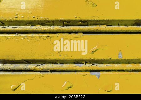 Background of old metal sheet with peel paint texture surface. Painted metal roller shutters door with peeling paint dirty yellow hue. Grungy backgrou Stock Photo