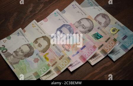 Row of new Ukrainian money with portraits of Ukrainian historical figures, face value 20, 100, 200, 500 and 1000 hryvnia. Paper cash on a wooden table Stock Photo