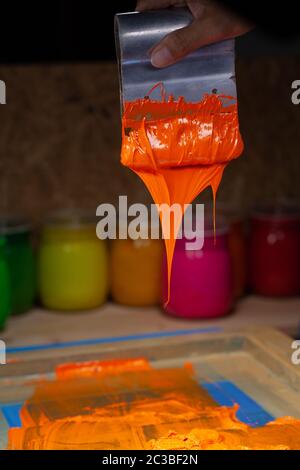 orange color dripping from hand screen printing during printing tee shirt  in tee shirt factory. Stock Photo