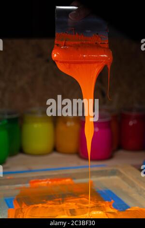 orange color dripping from hand screen printing during printing tee shirt  in tee shirt factory. Stock Photo