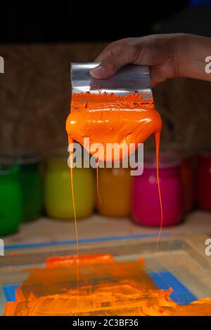 orange color dripping from hand screen printing during printing tee shirt  in tee shirt factory. Stock Photo