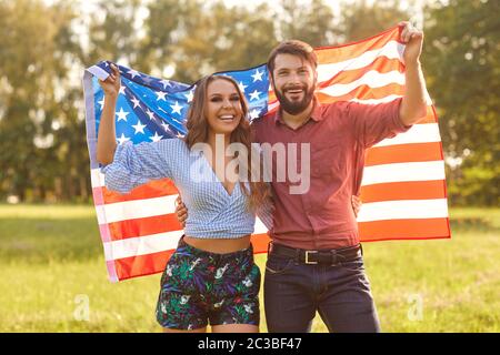 Happy couple with American flag outdoors. Young man and his girlfriend with national banner celebrating Independence Day Stock Photo