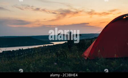 Girl near the tent at sunset with hands up. Stock Photo