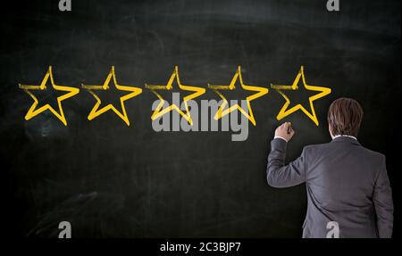 Businessman paints with chalk five stars on blackboard. Stock Photo