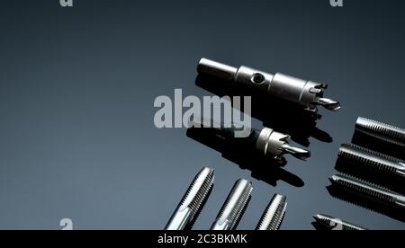 Closeup straight flute tap tip and hole saw on dark background.  Industrial tapping tools. Carbide tip metal cutter. Metalworking hardware. Mechanic t Stock Photo