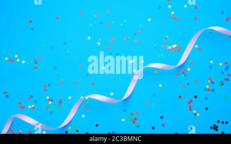 shiny multicolored round confetti scattered on a blue background and pink ribbon, festive backdrop for birthday, valentines day Stock Photo
