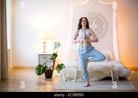 Smiling young brown haired woman in pajamas practicing yoga Stock Photo