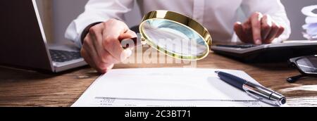 Auditor Analyzing Bill Through Magnifying Glass On Desk Stock Photo
