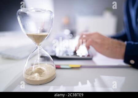 Hourglass In Front Of Businessperson Calculating Invoice Stock Photo