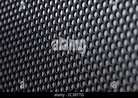 Macro shot of a black metal surface with round holes, gray background. Stock Photo