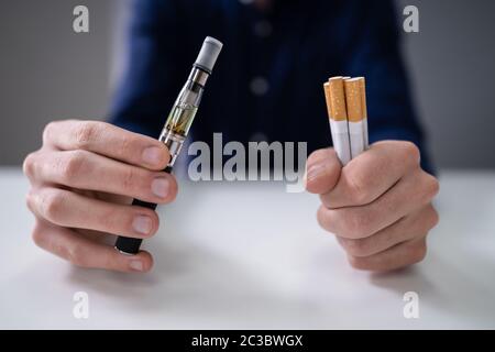 Man Holding Vape And Tobacco Cigarette Over Desk Stock Photo