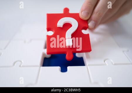 Close-up Of A Person's Hand Placing Red Question Mark Piece Into Jigsaw Puzzle Stock Photo