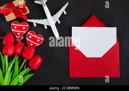 Red envelope with blank paper, airplane model, bouquet of tulips and gift box with hearts. Travel concept. Top view with space for your text. Top view Stock Photo