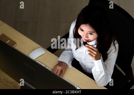 Late Night Environment. Top view of young adult friendly operator call center with headsets working hard at night. Using for 24 Hr. 7 days Call centre Stock Photo