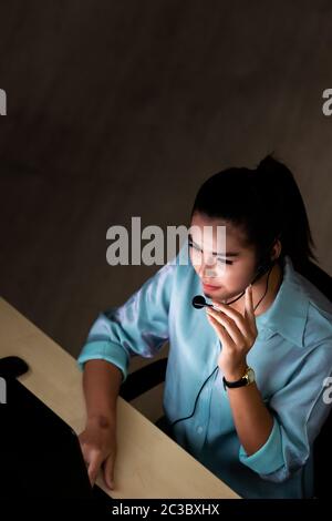 Late Night Environment. Top view of young adult friendly operator call center with headsets working hard at night. Using for 24 Hr. 7 days Call centre Stock Photo