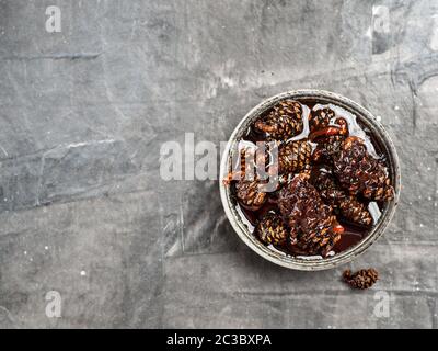 Delicious jam with baby pine cones in small bowl. Traditional Siberian dessert - young pine cones jam on gray textured background. Top view or flat la Stock Photo