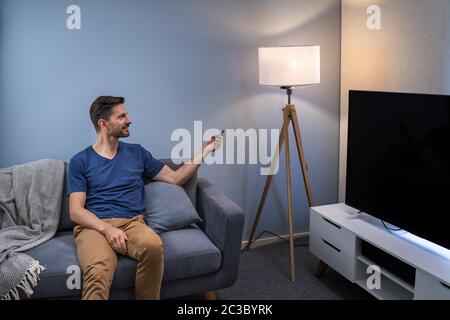 Person Controlling Smart Light With Remote Control Stock Photo