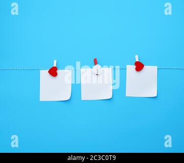 three empty square white paper sheets hanging on decorative clothespins, blue background Stock Photo