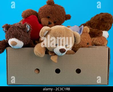 brown cardboard box with various teddy bears, blue background, concept of assistance and volunteering Stock Photo