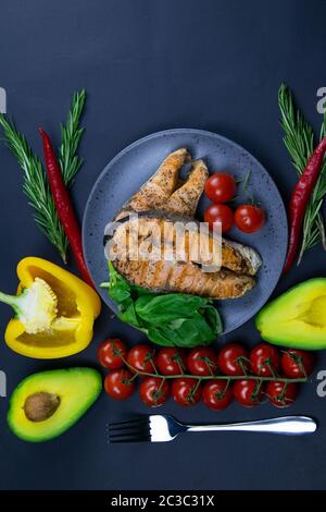Two fresh raw salmon steaks with vegetables and spices: rosemary, tomatoes, peppers, basil, lemon and olive oil on a gray plate on black background. T Stock Photo