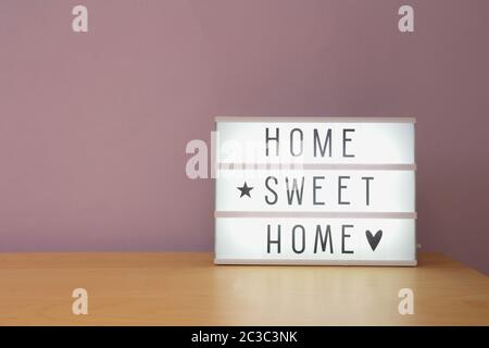 'Home sweet home' text in lighbox on wooden shelf, modern retro decoration purple wall Stock Photo