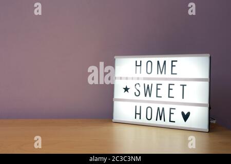 'Home sweet home' text in lighbox on wooden shelf, modern retro decoration purple wall Stock Photo