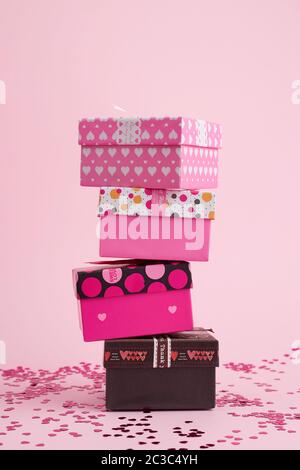 stack of cardboard square gift boxes on a pink background with shiny confetti, festive backdrop Stock Photo