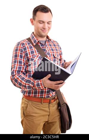 Portrait of a smiling young male student in stylish plaid shirt outfit with a shoulder bag holding and looking at an open notebook, isolated on white Stock Photo